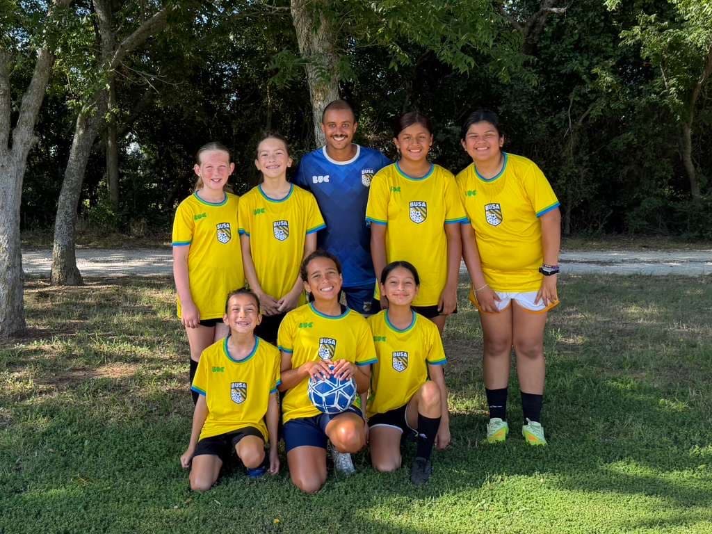 A youth girls futbol team posing with their coach after playing outdoors