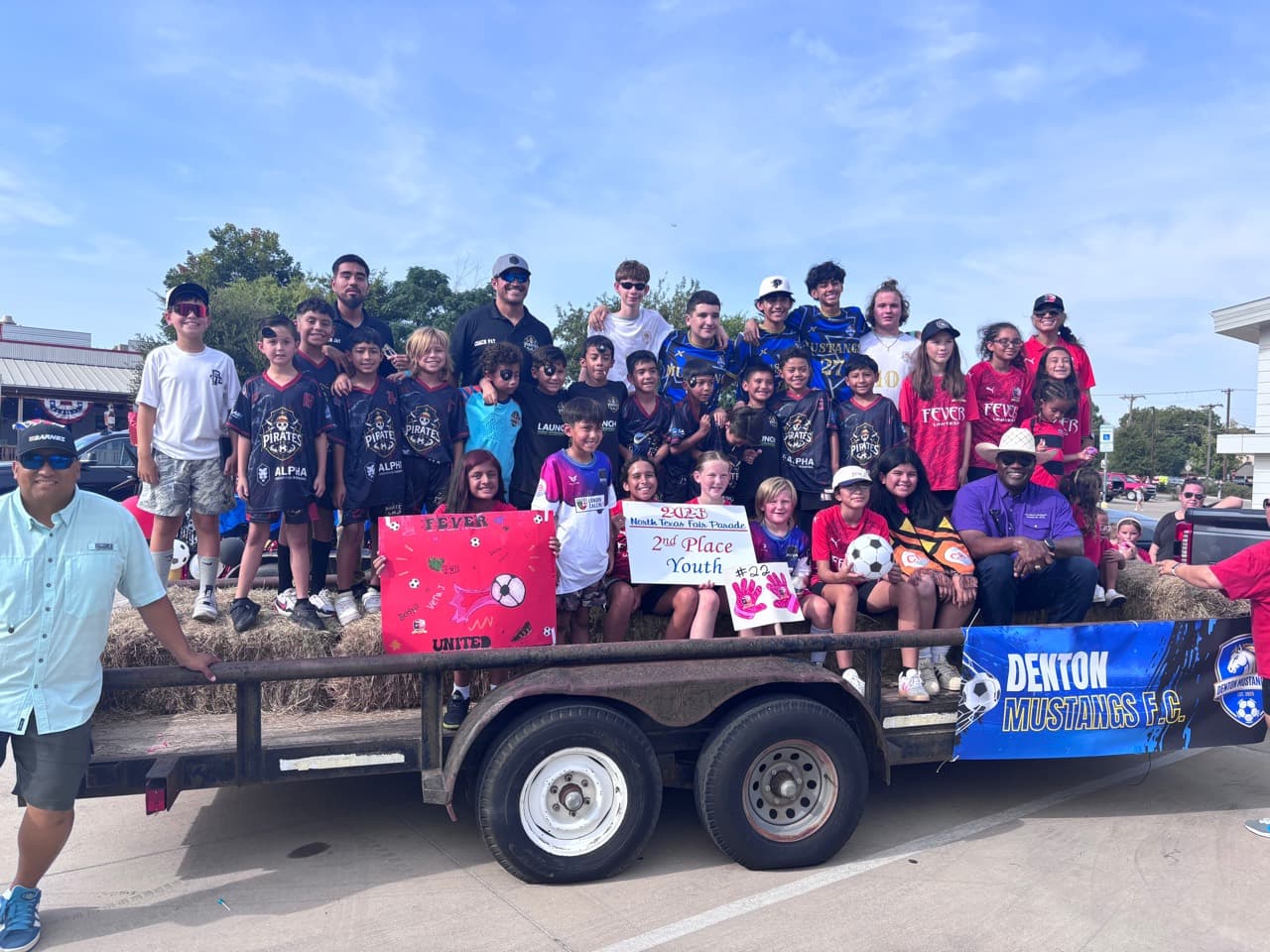 Youth futbol players and coaches from local clubs posing together on a parade trailer